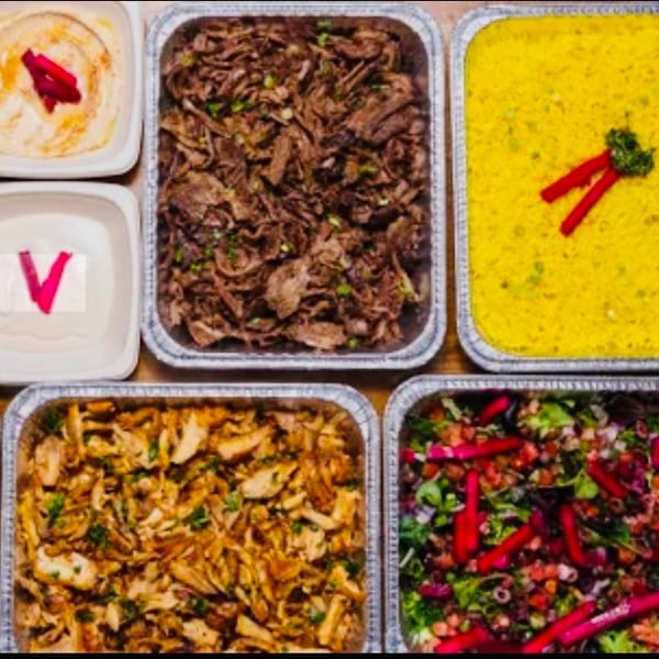 A catering spread of Middle Eastern food including pita, hummus, falafel, rice, meat, and salad.