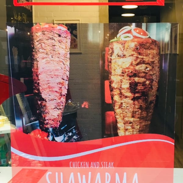 Restaurant window display advertising "Shawarma Non Stop" with images of two large shawarma spits.
