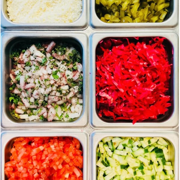 Six metal containers filled with various chopped ingredients like cheese, pickles, onions, cabbage, tomatoes, and cucumbers.